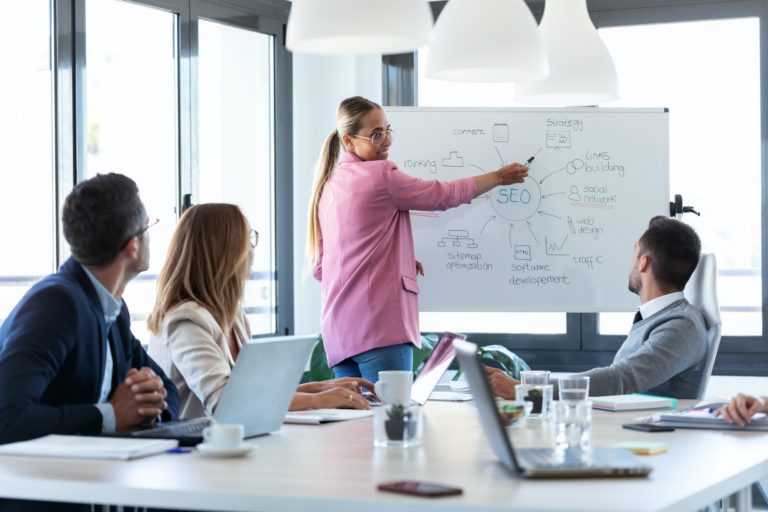 young businesswoman pointing at white blackboard and explain a project to her colleagues